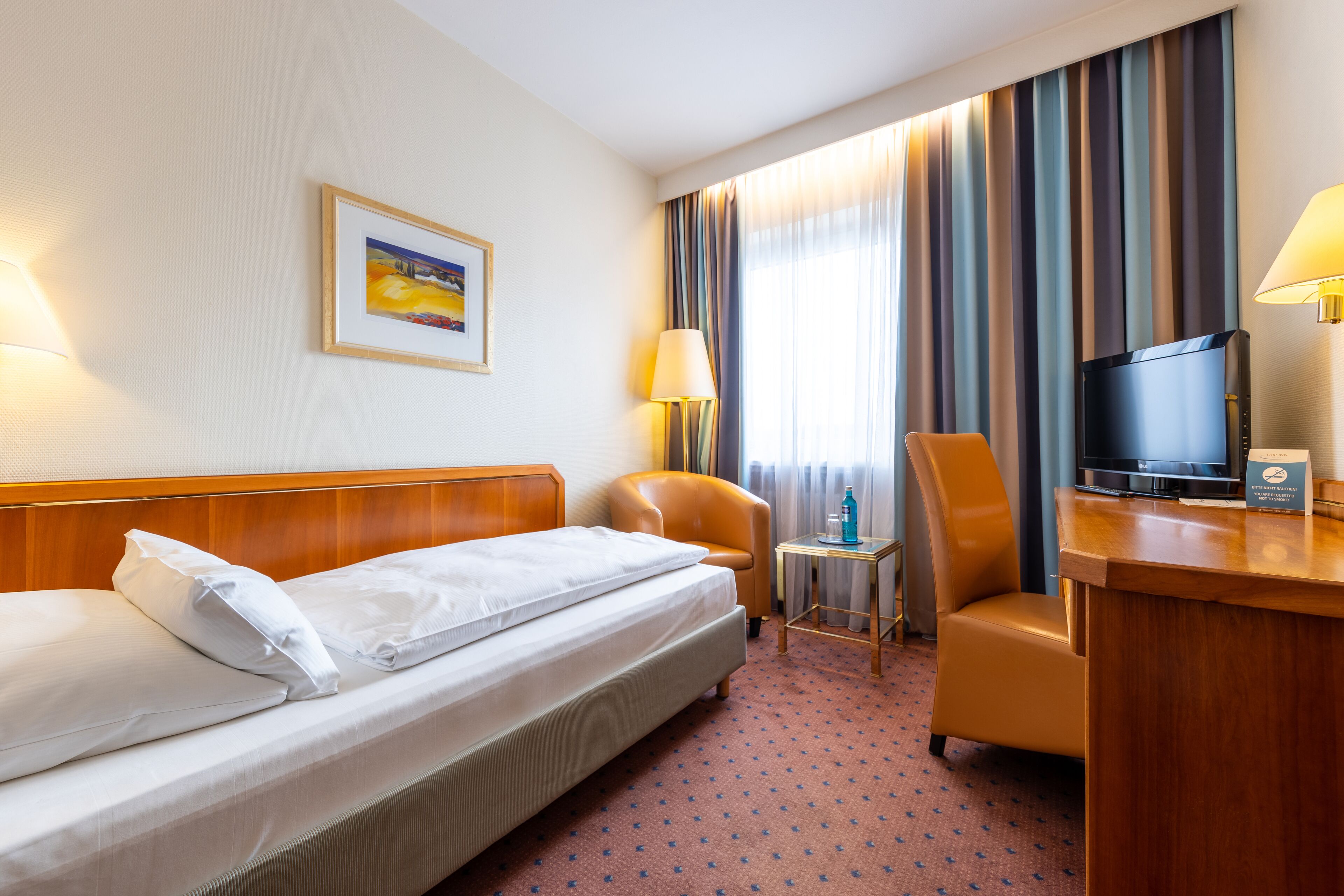 A hotel room with a bed, a desk, a chair, a television, and a lamp.