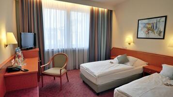 Habitación de hotel con dos camas, un escritorio con televisor, una silla y un cuadro en la pared.