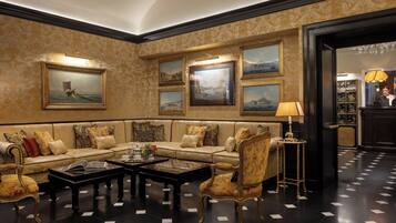 Un hall d’entrée luxueux, avec un papier peint à motifs, un ensemble de canapés, une table basse et des œuvres d’art encadrées accrochées au mur.