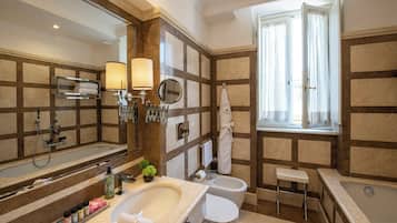 Un baño con un espejo grande, una bañera, un lavamanos y un inodoro. Hay una ventana con cortinas, un perchero para toallas y una planta pequeña en la encimera.