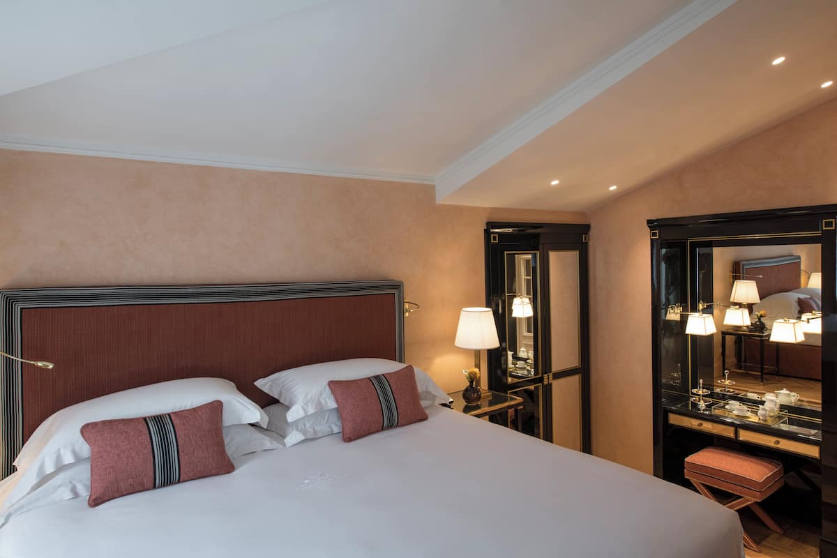A hotel room with a large bed, a nightstand with a lamp, a mirror, and a small table with a lamp.