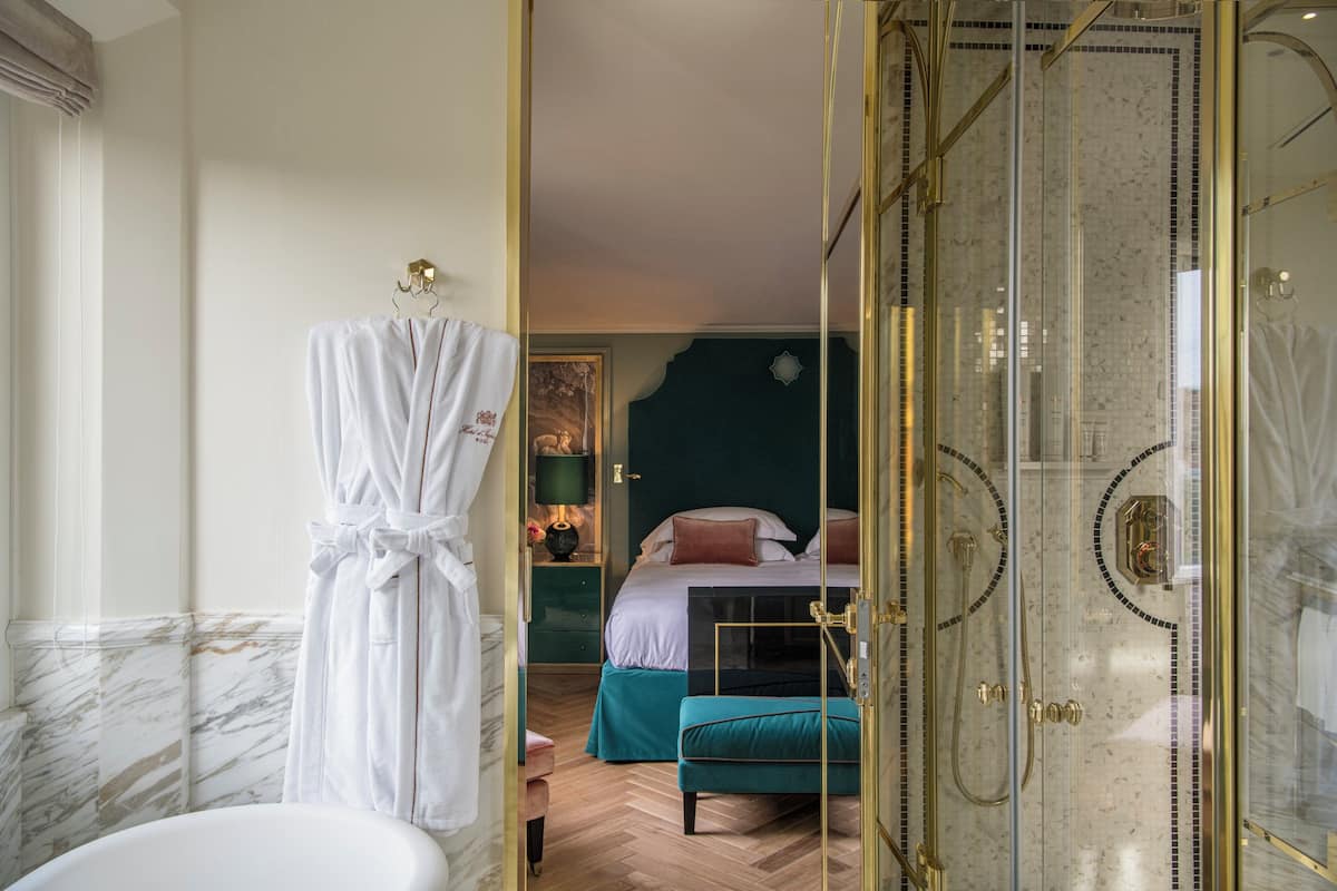 A bathroom with a marble wall, a white bathtub, and a white robe hanging on a hook.