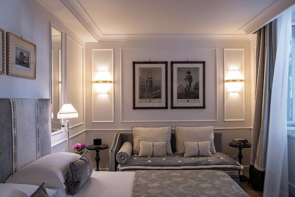 A hotel room with a large bed, a sofa, two framed pictures on the wall, and a lamp on either side of the bed.