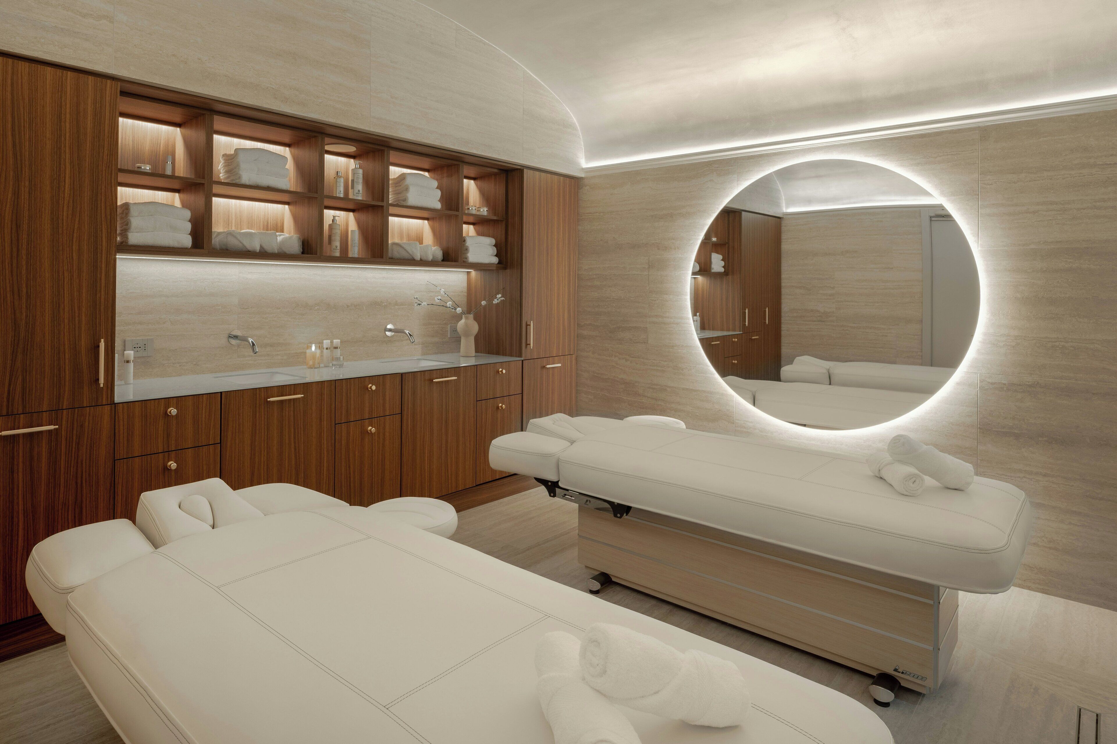 A modern spa room with wooden cabinets, a large mirror, and two massage tables.