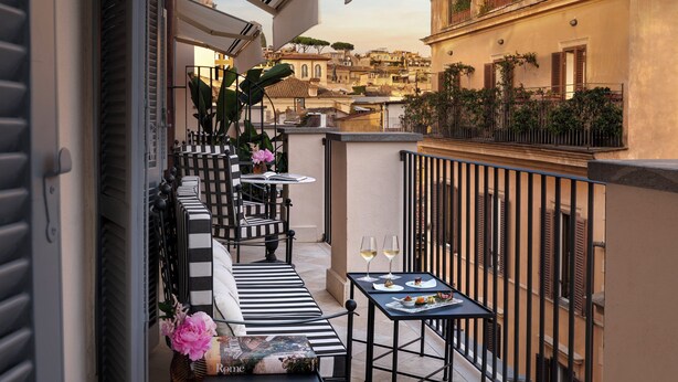 A balcony with a black and white striped sofa, a small table with two wine glasses, and a wicker basket with flowers. - Hotel d'Inghilterra Roma - Starhotels Collezione (Rome)