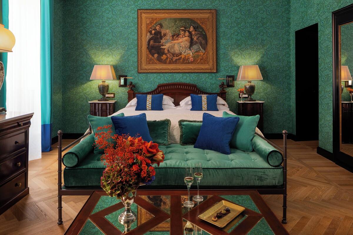 A bedroom with a green upholstered sofa, a wooden bed frame, a painting above the bed, and two bedside lamps.