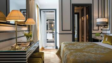 A hotel room with a large bed, a desk with lamps, and a mirror. There is a door leading to a bathroom and a hallway.
