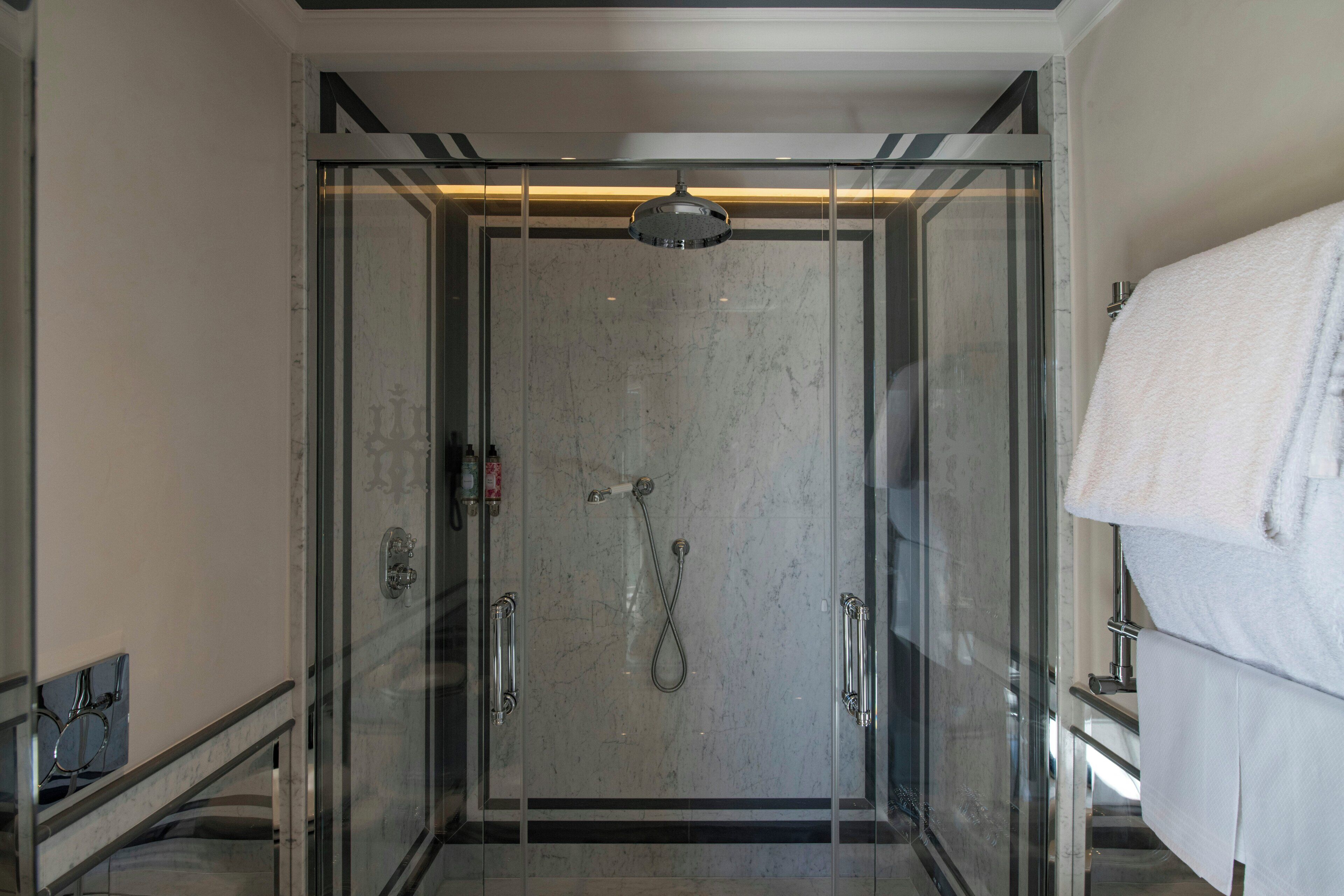 A glass-enclosed shower with a handheld showerhead, a towel rack, and a glass door.
