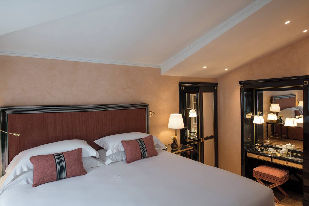 A hotel room with a large bed, a nightstand with a lamp, a mirror, and a small table with a lamp.