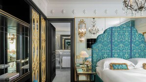 A hotel room with a large bed, a vanity with a mirror, a chandelier, and a view of the bathroom. - Hotel d'Inghilterra Roma - Starhotels Collezione (Rome)