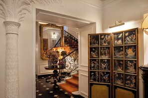A grand staircase with a black and white checkered floor, a decorative mirror, and a wall with framed botanical artwork.