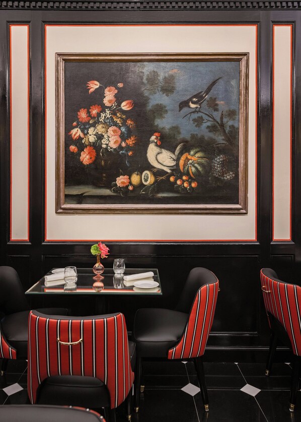 Un coin repas avec une table dressée pour deux personnes, agrémenté de chaises à rayures et d’un tableau encadré au-dessus.