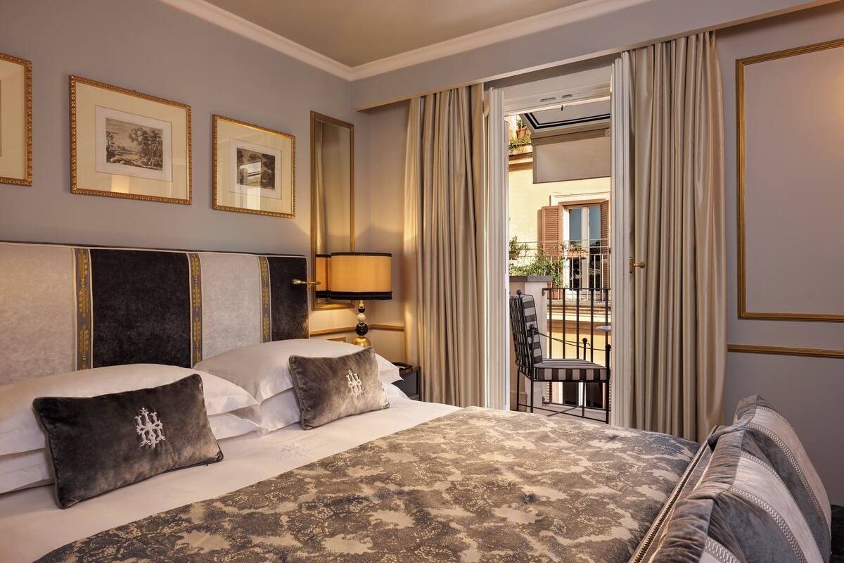 A hotel room with a large bed, a nightstand with a lamp, a view of the outside balcony, and framed pictures on the wall.