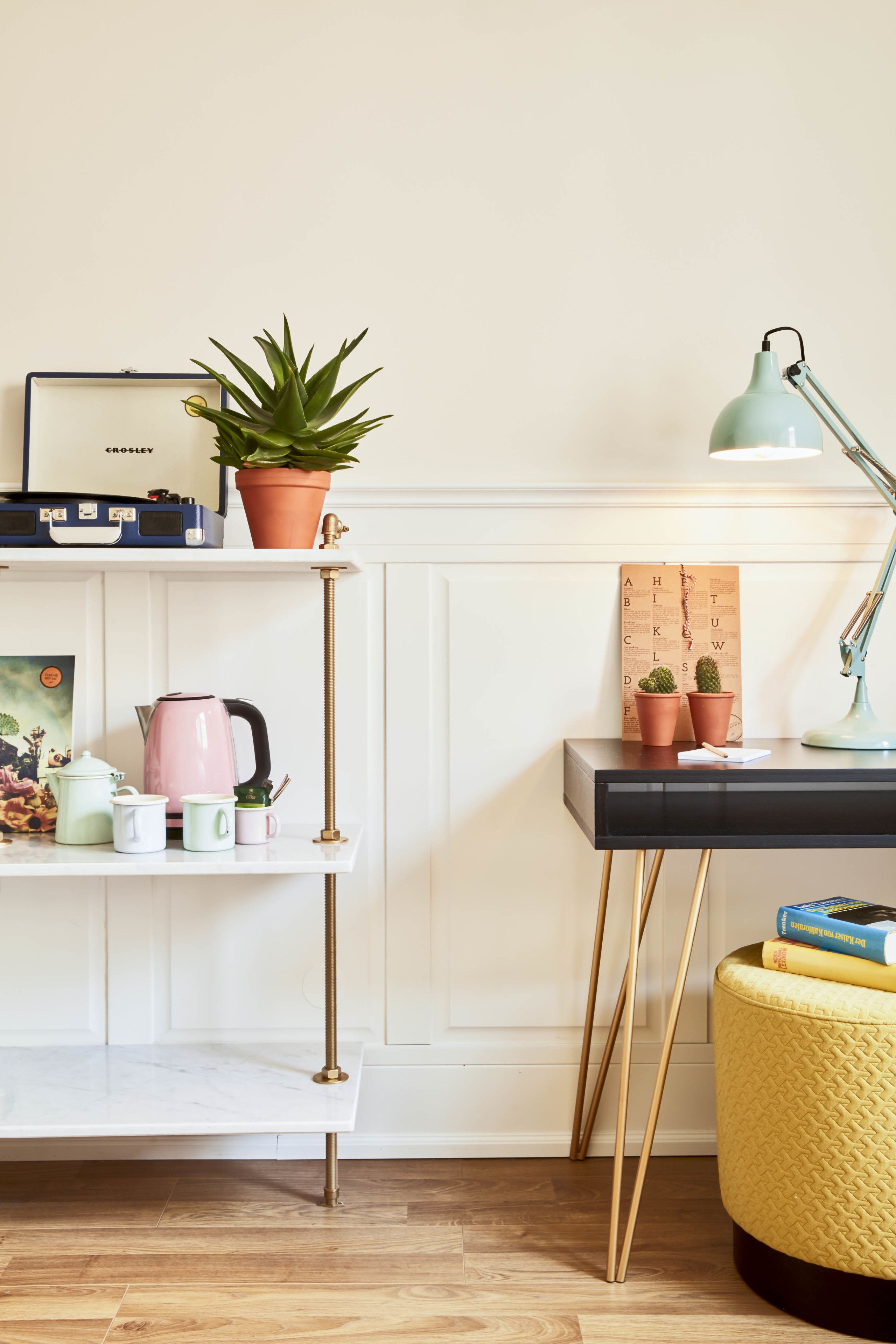Une pièce bien rangée, avec un meuble blanc, une étagère sur laquelle se trouve une radio ancienne, une bouilloire rose et une petite plante en pot.