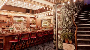 A bar area with wooden furniture, red chairs, and a staircase with a floral wall design.
