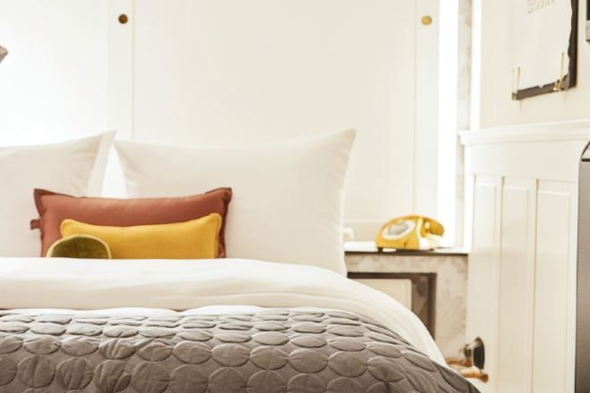 A neatly made bed with a grey quilt and multiple pillows in white, yellow, and brown.