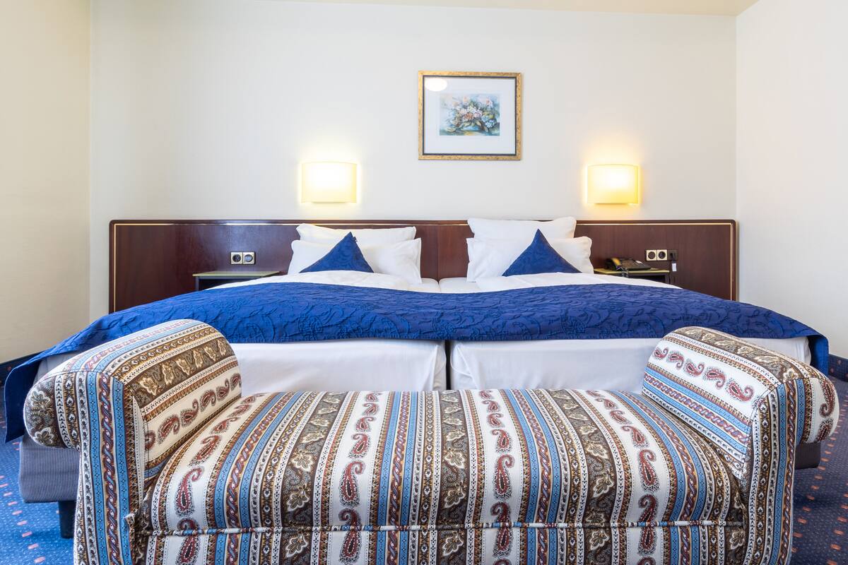 A hotel room with a large bed, two bedside lamps, a framed picture on the wall, and a patterned sofa.