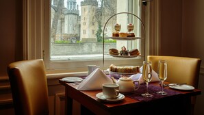 A dining table with a three-tiered dessert stand, a teapot, cups, and a glass of champagne.