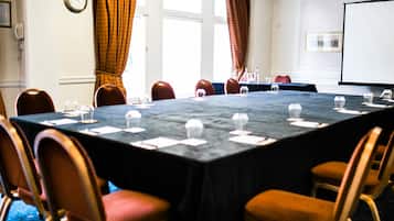 A conference room with a long table, chairs, a projector screen, and a clock on the wall.