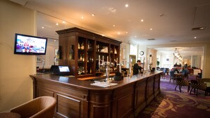 A bar area with a wooden counter, bar stools, and a television mounted on the wall.