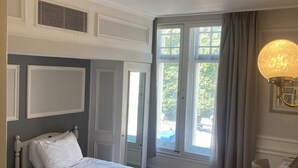 A hotel room with a double bed, a desk with a lamp, a window with curtains, and a view of the outdoors.