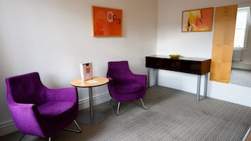 Una habitación moderna con dos sillas moradas, una mesita redonda pequeña y un mueble aparador de madera oscura con un cuenco.