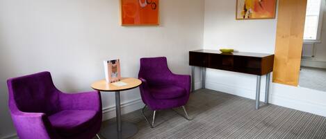 A modern room with two purple chairs, a small round table, and a dark wooden console table with a bowl.