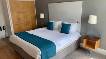 A hotel room with a large bed, a wooden wardrobe, two bedside lamps, and a small wooden side table.