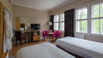 Quarto de hotel com duas camas, uma escrivaninha com computador, televisão, uma cadeira e janelas amplas.