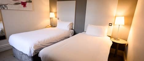 A hotel room with two beds, each with a bedside table and lamp.