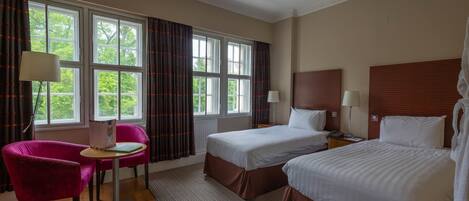 A hotel room with two beds, a desk with a chair, and large windows with curtains.