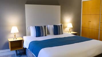 A hotel room with a large bed, two bedside tables with lamps, a wardrobe, and a headboard.
