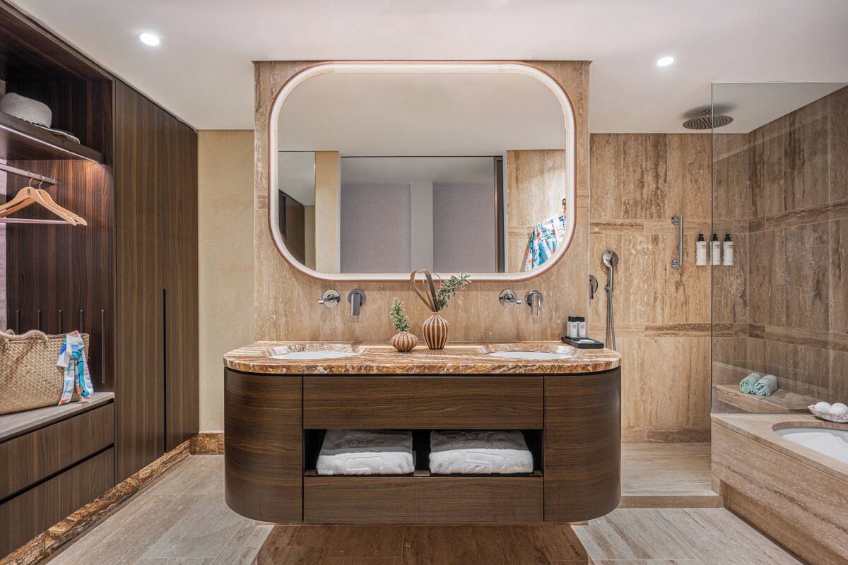 A modern bathroom with a large mirror, dual sinks, and a walk-in shower.