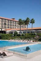 Un hotel con piscina, sillas de descanso, palmeras y techo de tejas.
