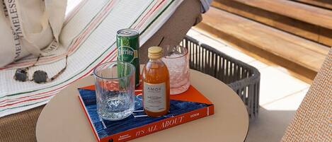 A lounge area with a striped towel, a book titled "It's All About," and a bottle of Amor.