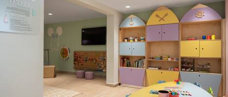 A children's playroom with colorful cabinets, a play area, and a table with toys and books.