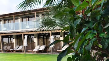 Een hotel met een overdekt terras, een verzorgd gazon en weelderige begroeiing.