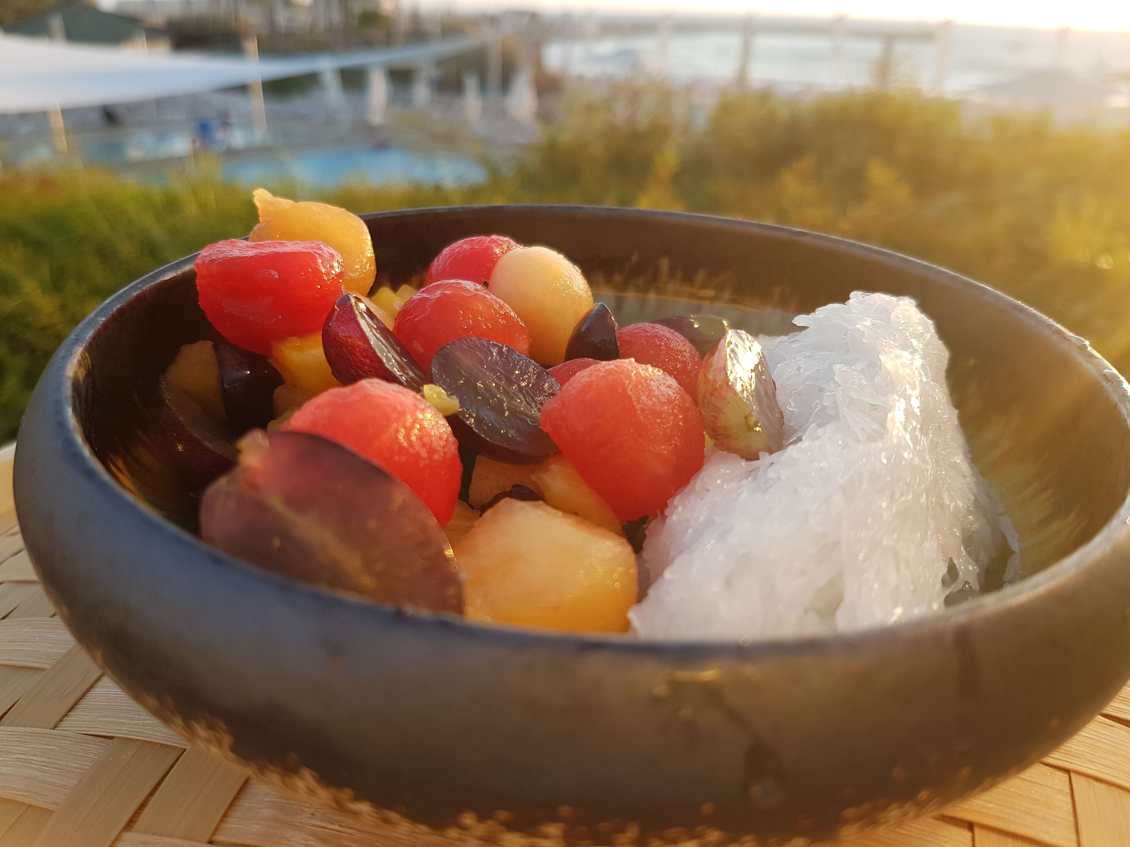 A bowl of fruit with ice on a woven surface.