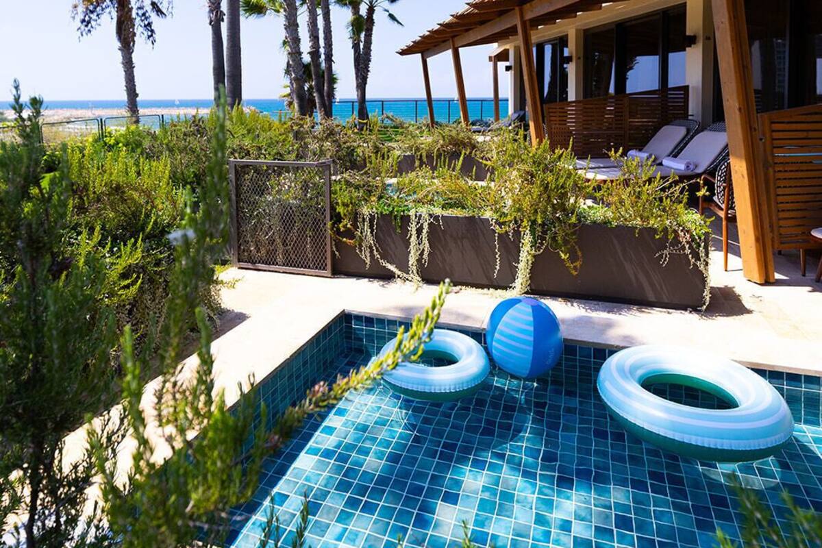 A pool area with a view of the ocean, surrounded by palm trees and a wooden pergola.