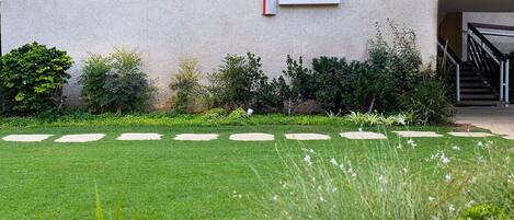 Fachada moderna de edificio con arte mural geométrico y un jardín cuidado con piedras para caminar.