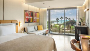 A hotel room with a large bed, a sofa, a dining area, and a balcony with a view of the ocean. - Dan Accadia Hotel (Herzliya)