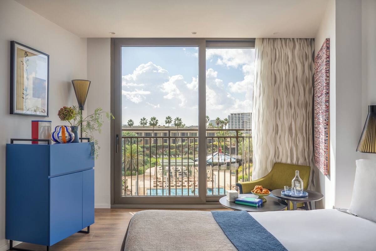 A hotel room with a large balcony, a bed, a desk, and a chair.