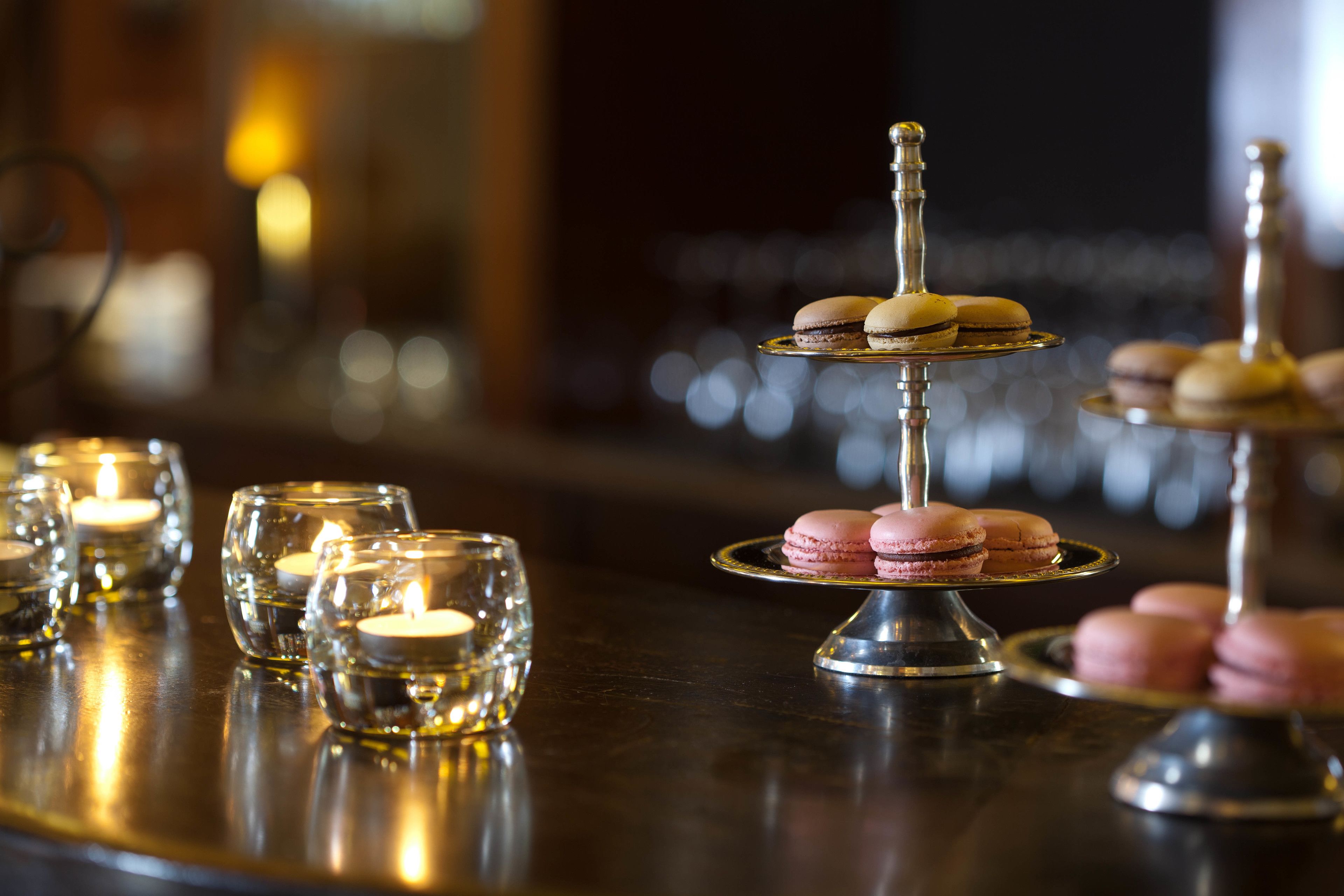 A bar setting with a tiered dessert stand featuring macarons, lit candles, and a reflective surface.