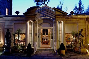 A grand entrance with a central archway, flanked by columns and statues, leading to a warmly lit interior.
