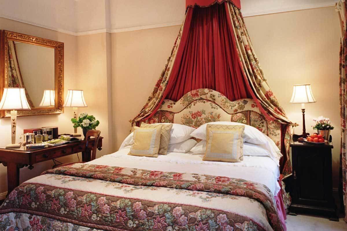 A bedroom with a canopy bed, floral bedding, a desk with lamps, and a mirror.