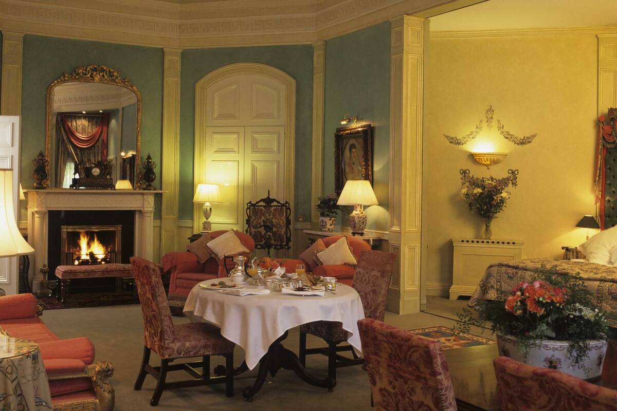 A formal dining room with a fireplace, a round table set for four, and a comfortable seating area with armchairs and sofas.