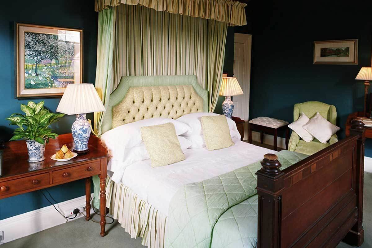 A bedroom with a large bed, green curtains, and a nightstand with a lamp.