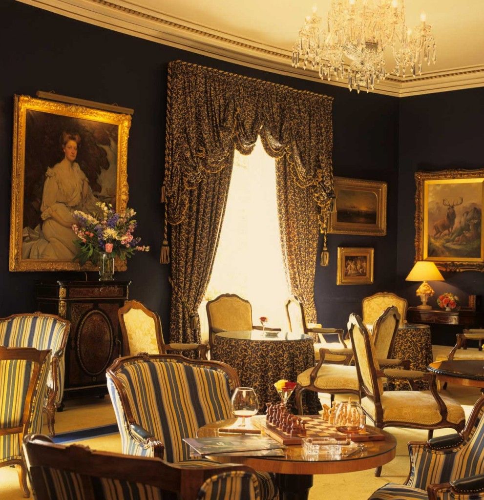 A room with a chandelier, a large window with curtains, and multiple framed pictures on the walls.