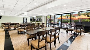 Un vaste espace de restauration intérieur, doté de nombreuses tables et chaises, de grandes fenêtres offrant une vue sur l’extérieur et d’un sol carrelé.