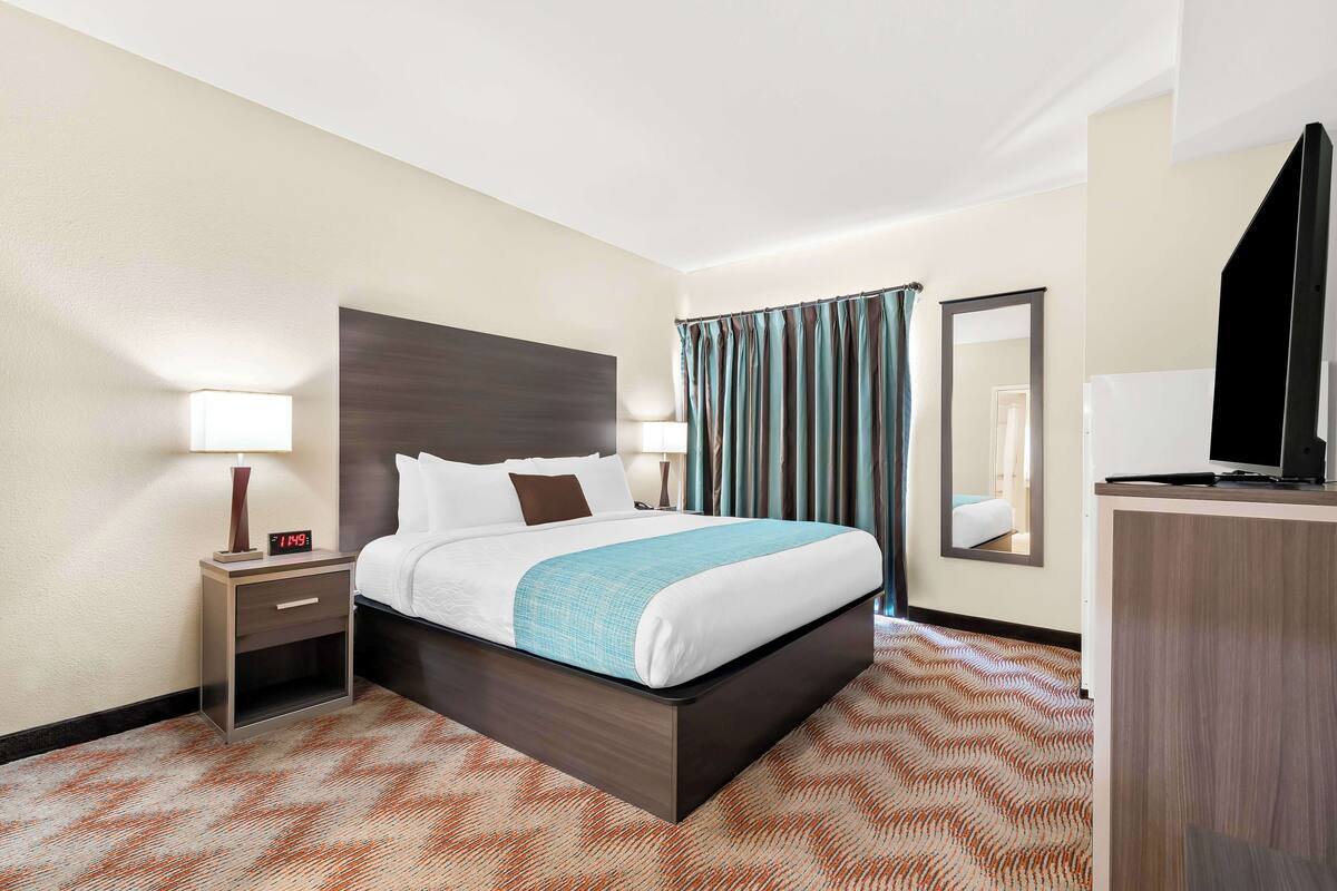 A hotel room with a bed, bedside table, lamp, and a mirror.